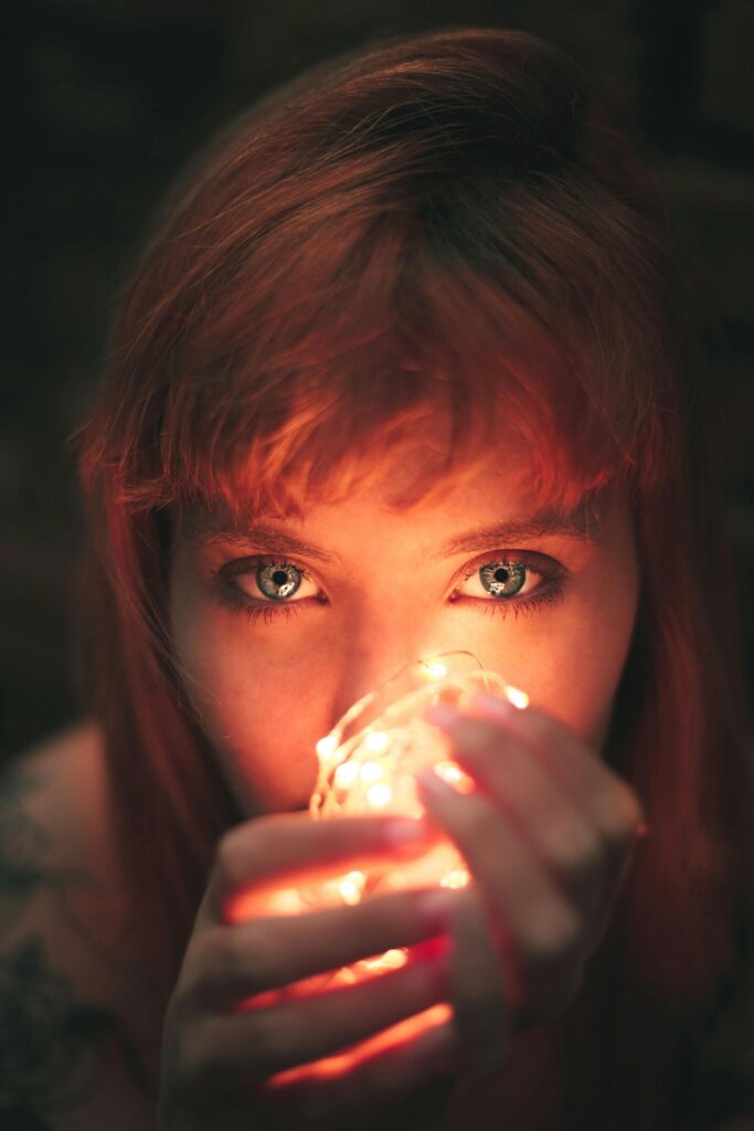 Artistic portrait of a red-haired woman holding fairy lights, creating a warm and moody atmosphere.