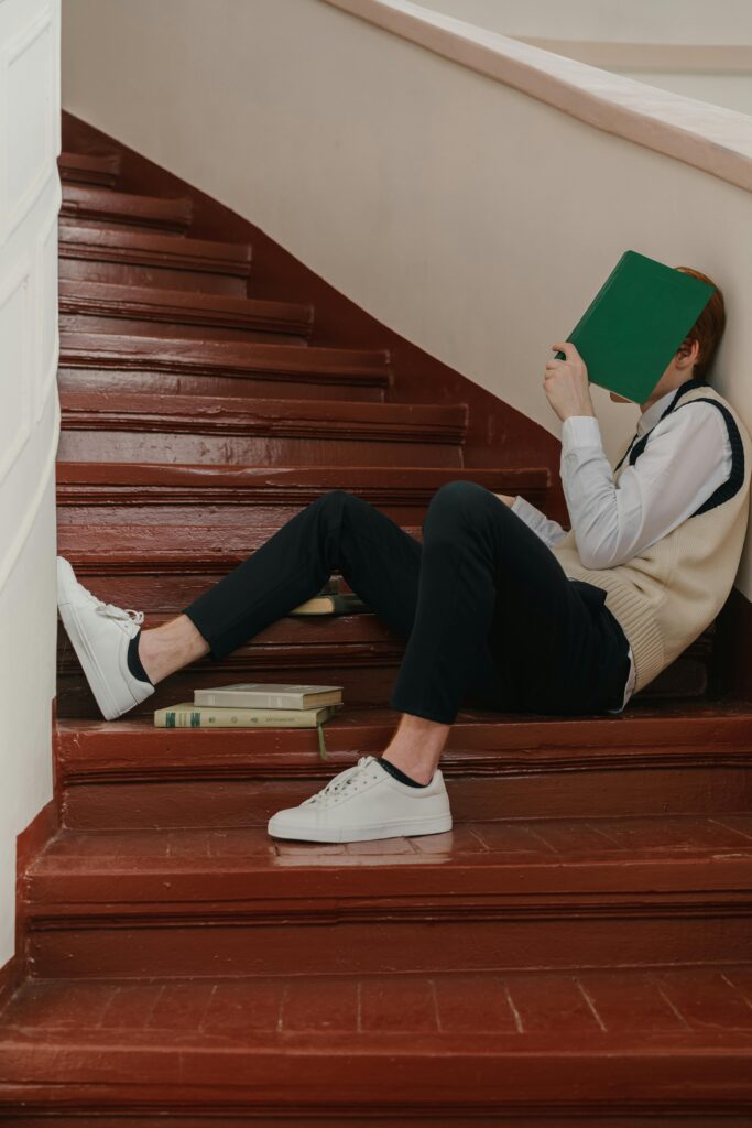 Student in a uniform reading on staircase, symbolizing education and learning environment.